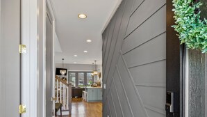 A hallway with wooden flooring, a dark gray wall, and a black door with a green plant decoration. - Gorgeous Lake House in Twin Creeks - Marina Side (Winchester)