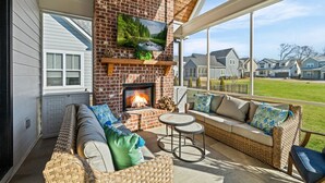 A cozy outdoor seating area with a brick fireplace, wicker furniture, and a large window overlooking a residential neighborhood. - Gorgeous Lake House in Twin Creeks - Marina Side (Winchester)