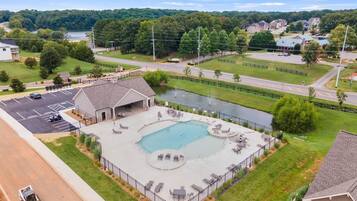 A swimming pool with lounge chairs and a covered patio area, surrounded by a fence and a parking lot.