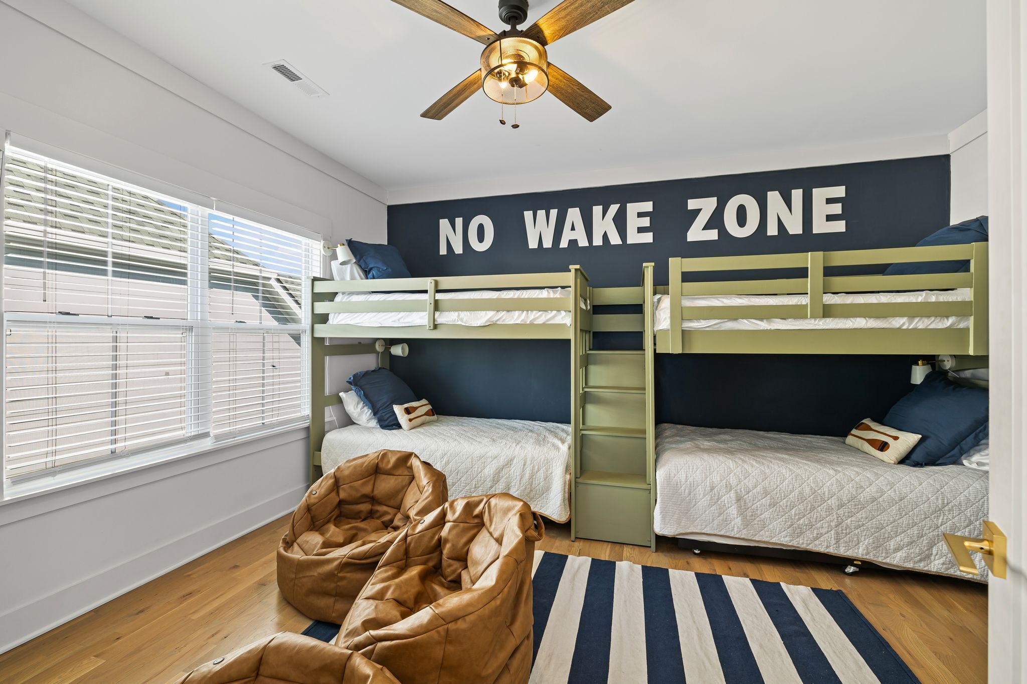 A room with bunk beds, a 'NO WAKE ZONE' sign, a bean bag chair, and a ceiling fan.