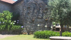 A stone building with a tiled roof, surrounded by a well-maintained garden with various plants and flowers.