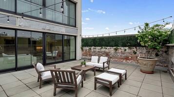 An outdoor patio area with a seating arrangement, a potted plant, and a brick wall.