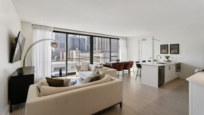 Un appartement moderne comprenant un salon, un coin repas et une cuisine, avec de grandes fenêtres offrant une vue sur la ville.