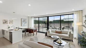 A modern apartment with a kitchen, dining area, and living room, featuring large windows and a view of the cityscape.
