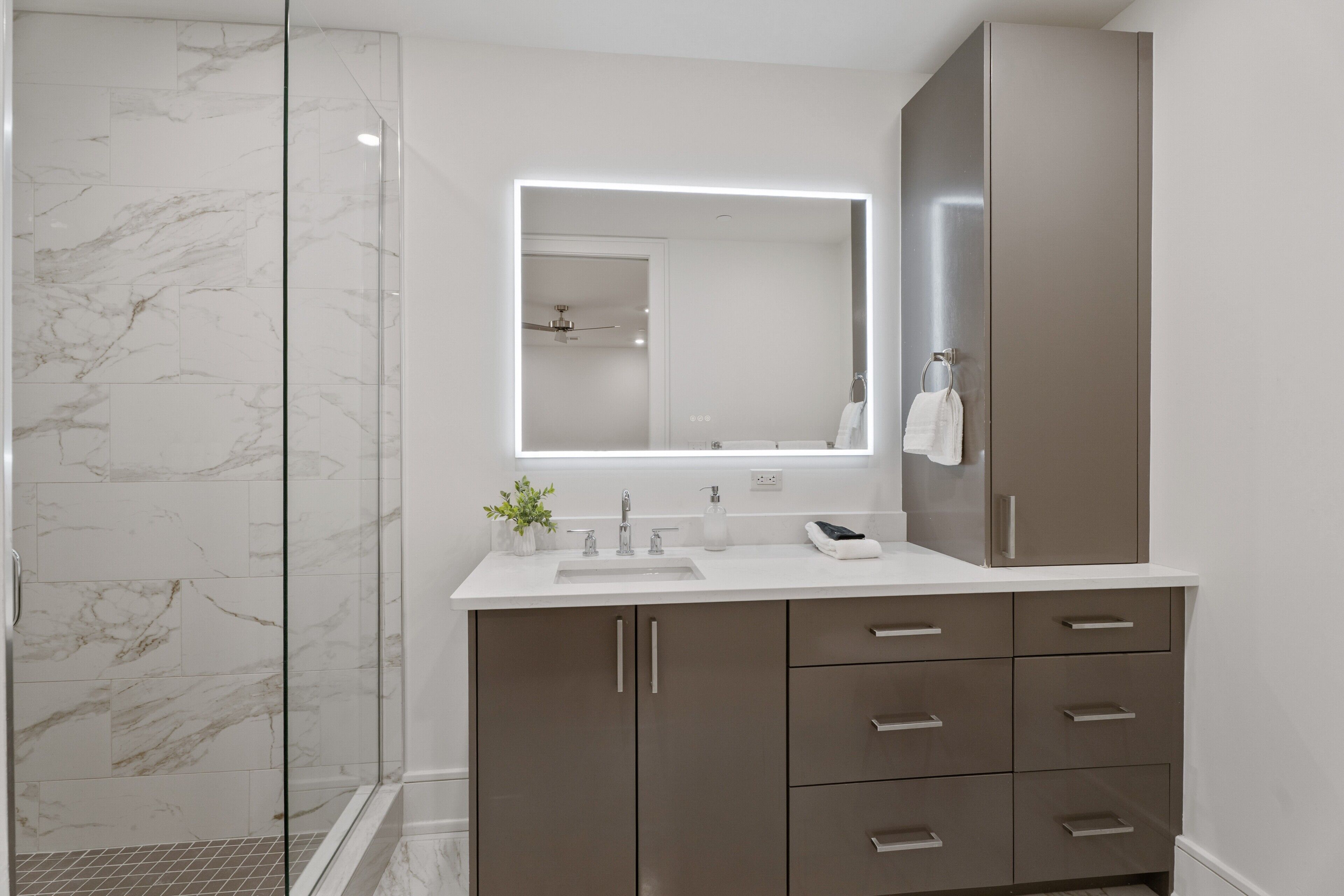 Une salle de bain moderne dotée d’une douche à parois de verre, d’un grand miroir et d’un meuble-lavabo avec des tiroirs.