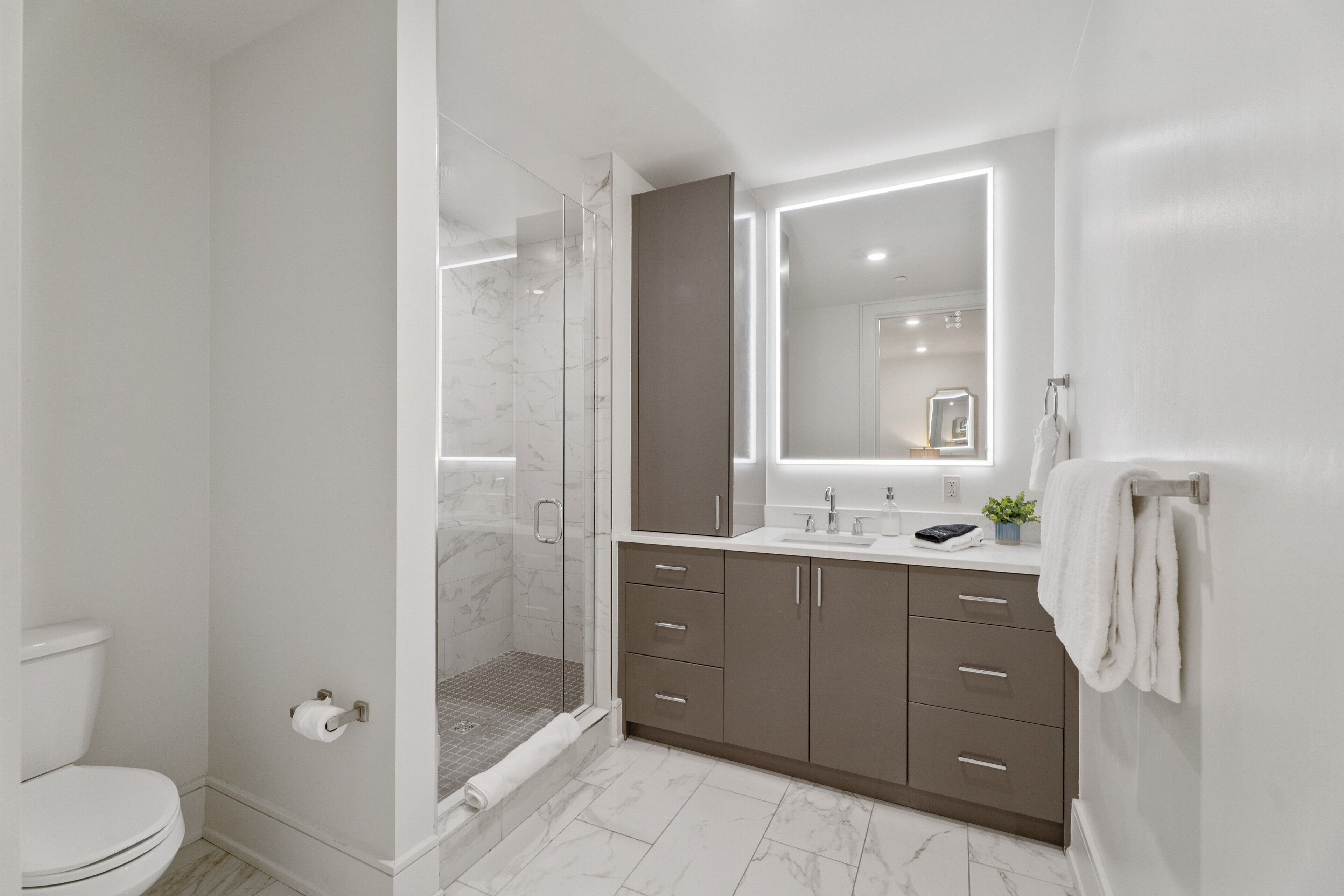 Une salle de bain moderne avec une douche à parois de verre, des toilettes et un meuble-lavabo doté de tiroirs et d’un miroir.