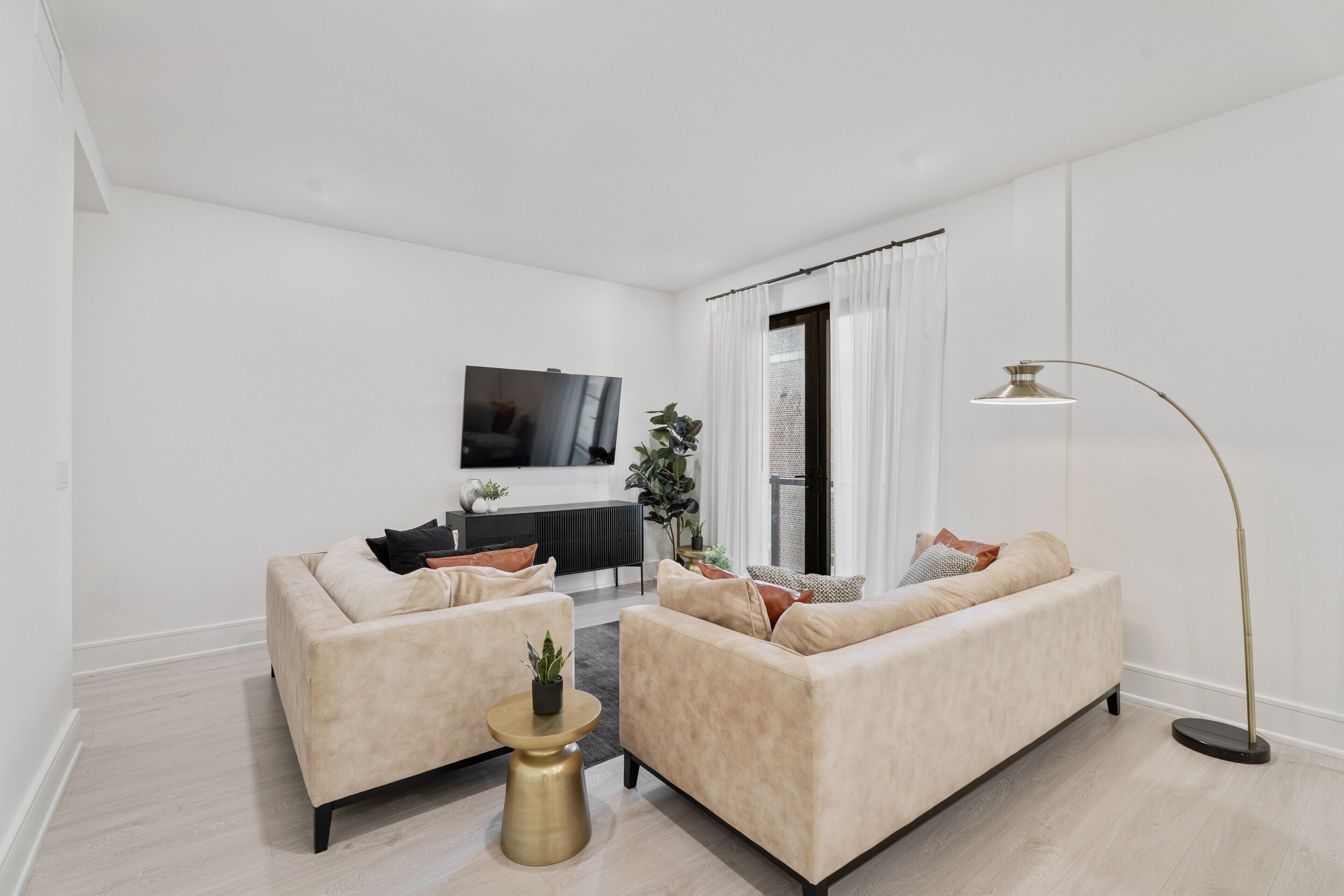 A modern living room with a beige sofa set, a coffee table, a floor lamp, and a flat-screen TV mounted on the wall.