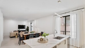 Une cuisine moderne dotée d’un plan de travail en marbre, un coin repas avec une table et des chaises, et un salon avec un canapé et une télévision.