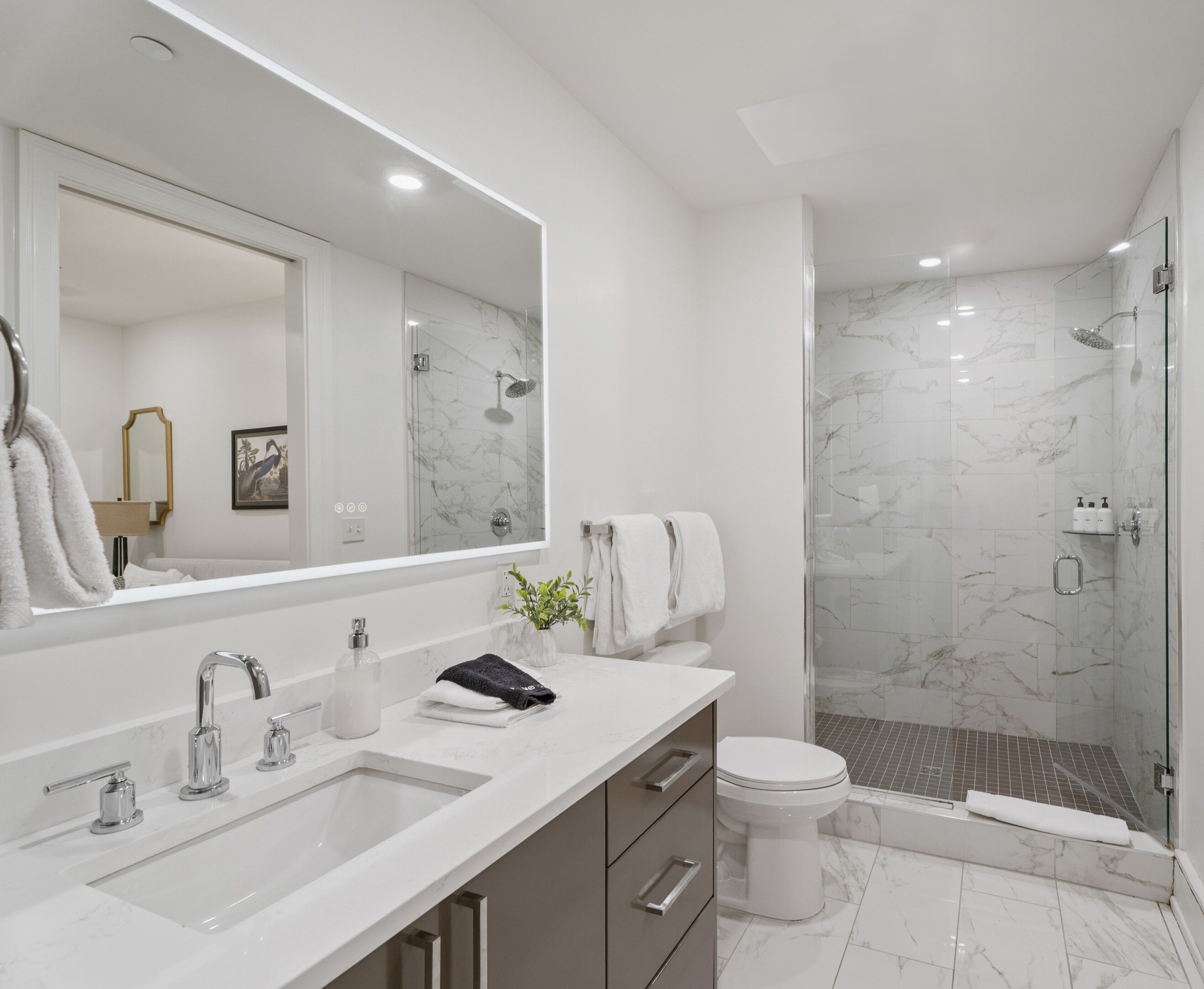 Une salle de bain moderne avec un grand miroir, un lavabo, des toilettes et un espace douche.