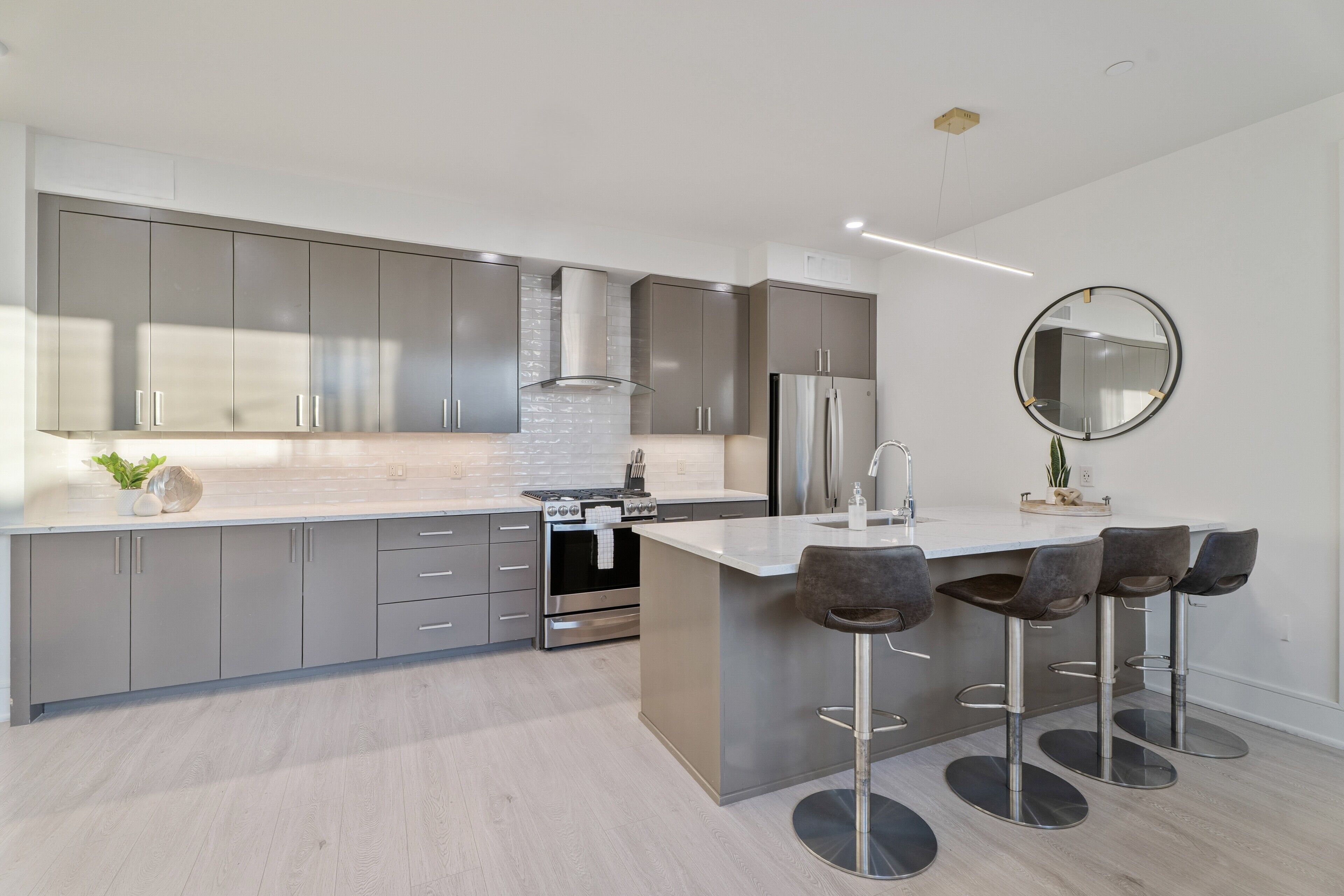 Una cocina moderna con armarios grises, un refrigerador de acero inoxidable y una isla central con taburetes de bar.