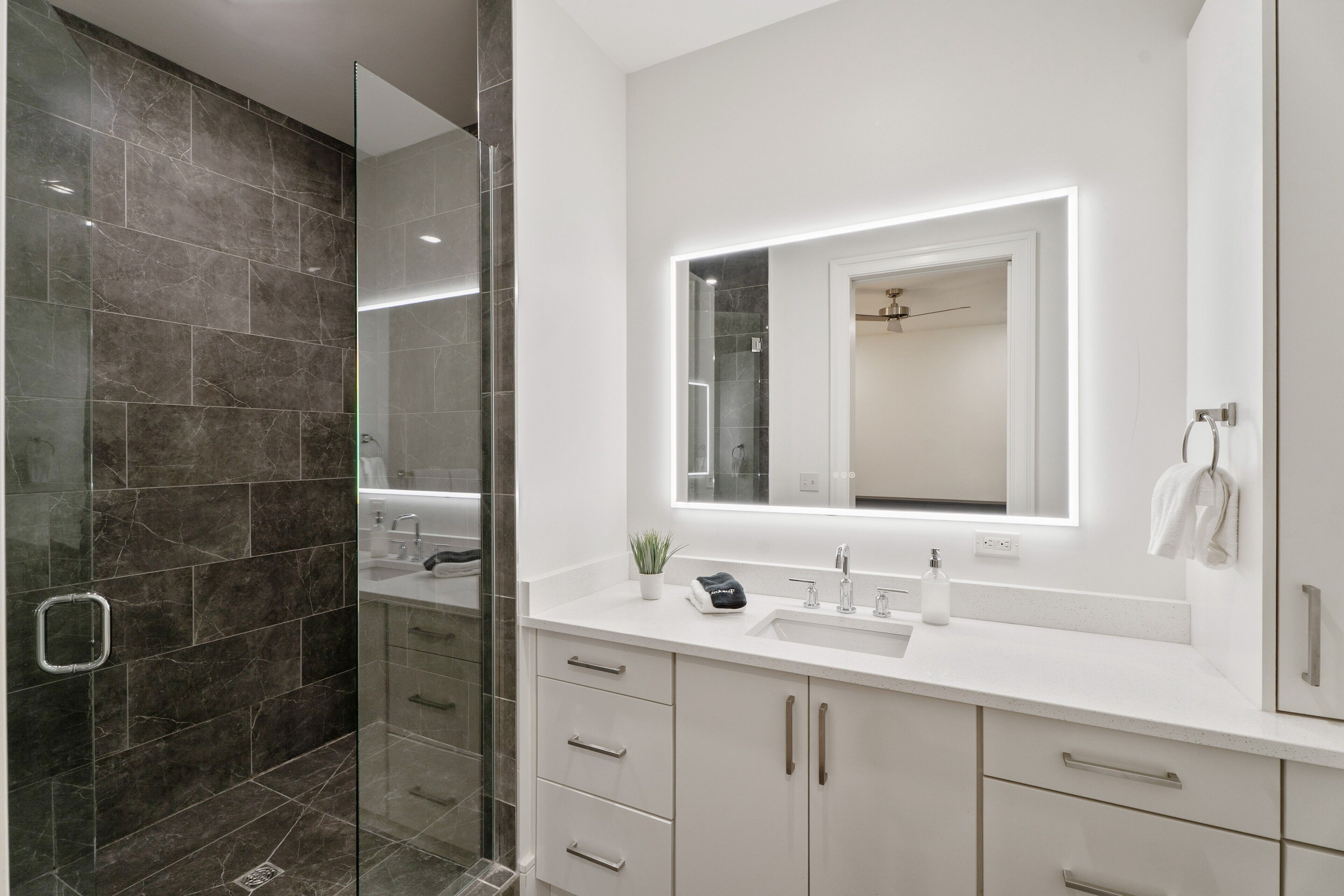 A modern bathroom with a glass shower enclosure, a white vanity with a large mirror, and a white sink.