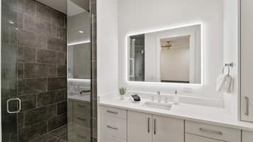 A modern bathroom with a glass shower enclosure, a white vanity with a large mirror, and a white sink.