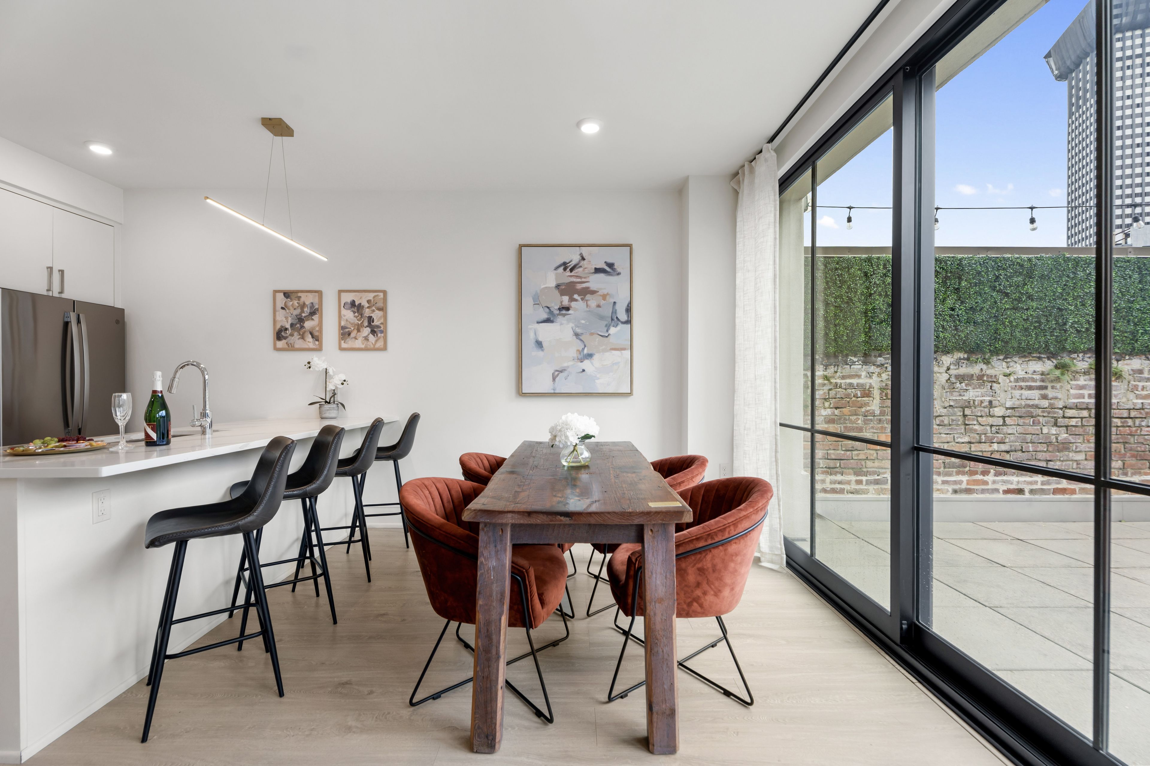 Una cocina moderna con comedor, que cuenta con un amplio ventanal con vistas a un muro de ladrillo y follaje.