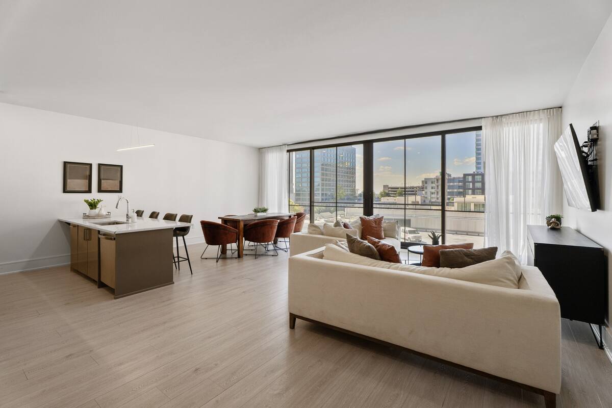 Una sala de estar moderna con un ventanal grande, un sofá, un comedor y una cocina.