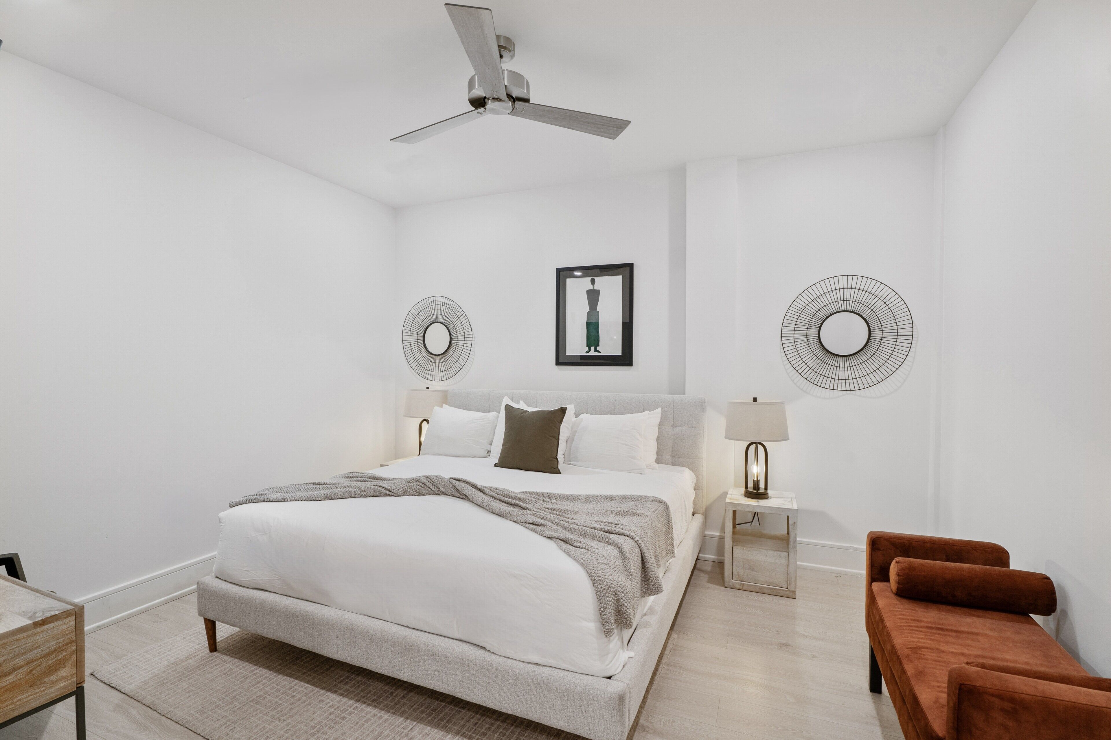 Une chambre à coucher moderne avec un grand lit, un ventilateur de plafond, deux lampes fixées au mur et un canapé marron.