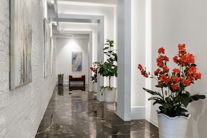 A hallway with a marble floor, white walls, and a bench. There are potted plants and a painting on the wall. - The Theodore New Orleans (New Orleans)