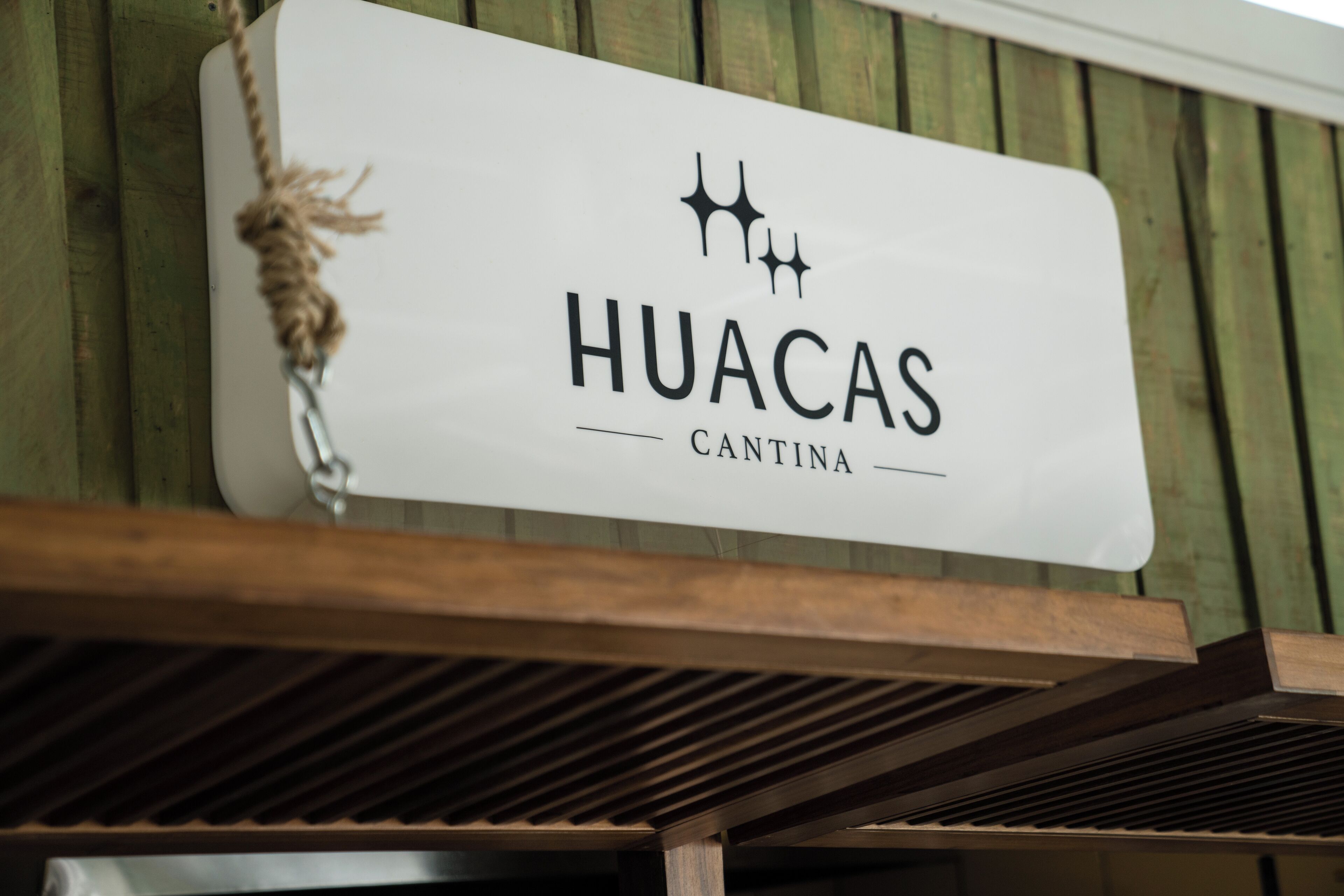 Un letrero con el texto 'HUACAS CANTINA' colgado de una estructura de madera.