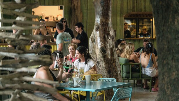 An outdoor seating area with tables and chairs, surrounded by trees. - The Beach Break Surf Hotel (Nosara)