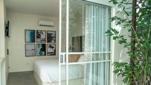 A bedroom with a bed, a sliding glass door, and a wall-mounted air conditioner. - The Beach Break Surf Hotel (Nosara)