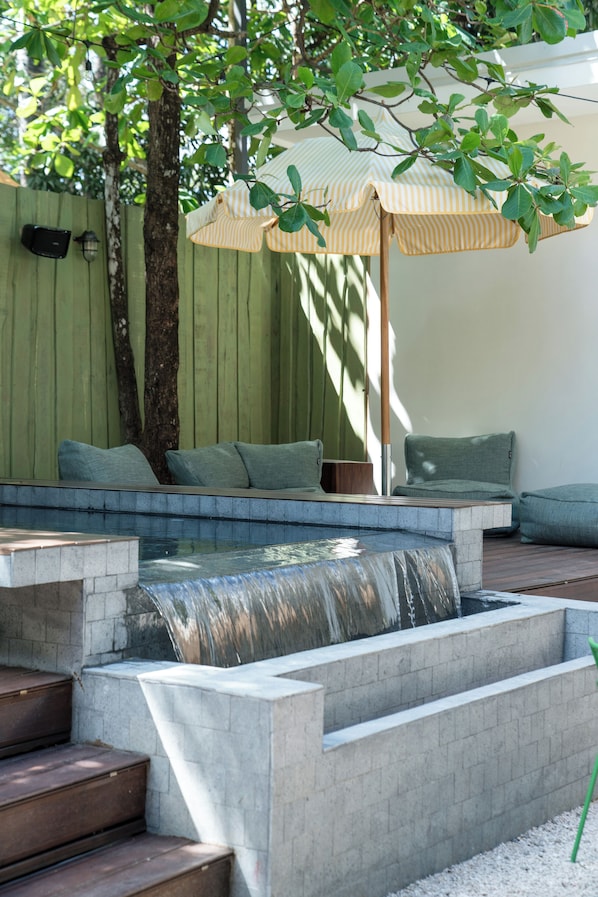 A modern outdoor seating area with a built-in water feature and a green fence in the background. - The Beach Break Surf Hotel (Nosara)