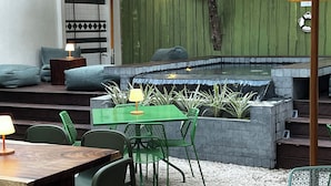 An outdoor seating area with a green table and chairs, a small hot tub, and a striped umbrella. - The Beach Break Surf Hotel (Nosara)