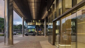 Un edificio moderno con fachada de vidrio, una columna metálica y un área de entrada pavimentada.