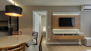 A modern living room with a round dining table, wooden chairs, a mounted TV, and a built-in entertainment unit. - Palazzo Torquetti Condo Hotel e Eventos (Belo Horizonte)