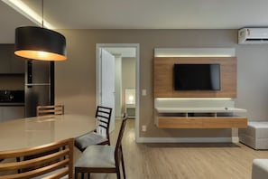 Un soggiorno moderno con un tavolo rotondo, sedie in legno, una TV a parete e un mobile TV a incasso.