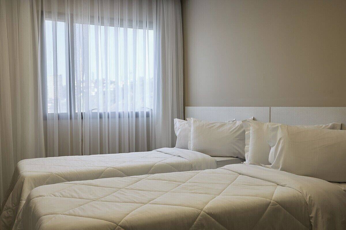 A hotel room with two beds, white bedding, a large window with sheer curtains, and a neutral color scheme.