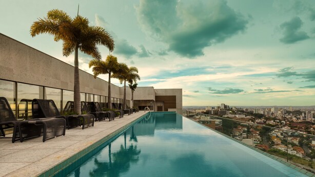 A rooftop infinity pool with lounge chairs and palm trees, overlooking a cityscape. - Palazzo Torquetti Condo Hotel e Eventos (Belo Horizonte)