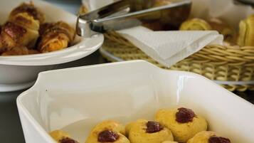Uma mesa de buffet com diversos alimentos, incluindo pastelaria e um prato branco com pastelaria redonda coberta com um produto vermelho.