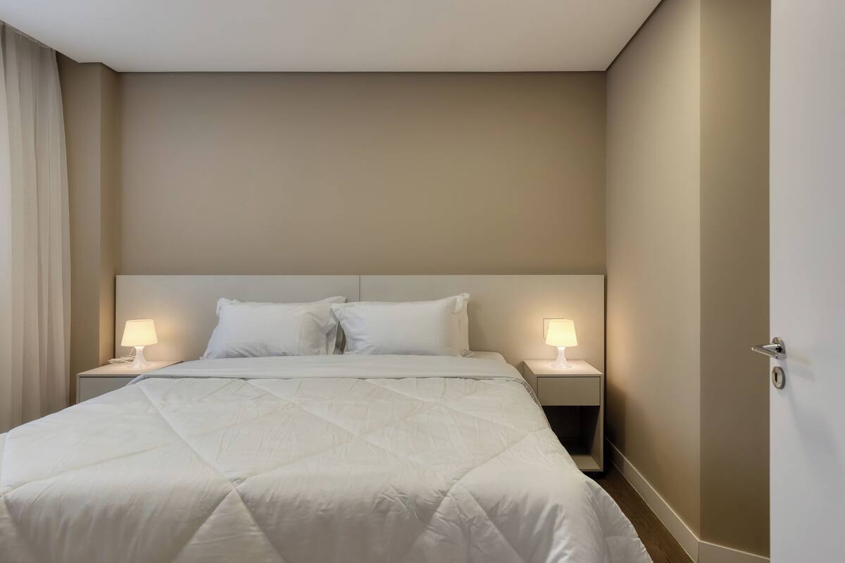 A hotel room with a large bed, two bedside lamps, and a door.