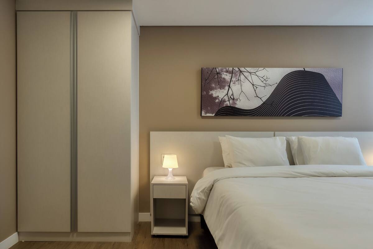 A bedroom with a bed, a nightstand with a lamp, a wardrobe, and a wall-mounted painting.