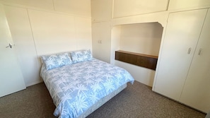 A bedroom with a bed, a wardrobe, and a built-in shelf.