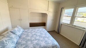 Een slaapkamer met een bed, hoofdeinde, raam en een kledingkast.
