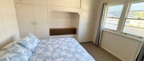 A bedroom with a bed, a headboard, a window, and a wardrobe.