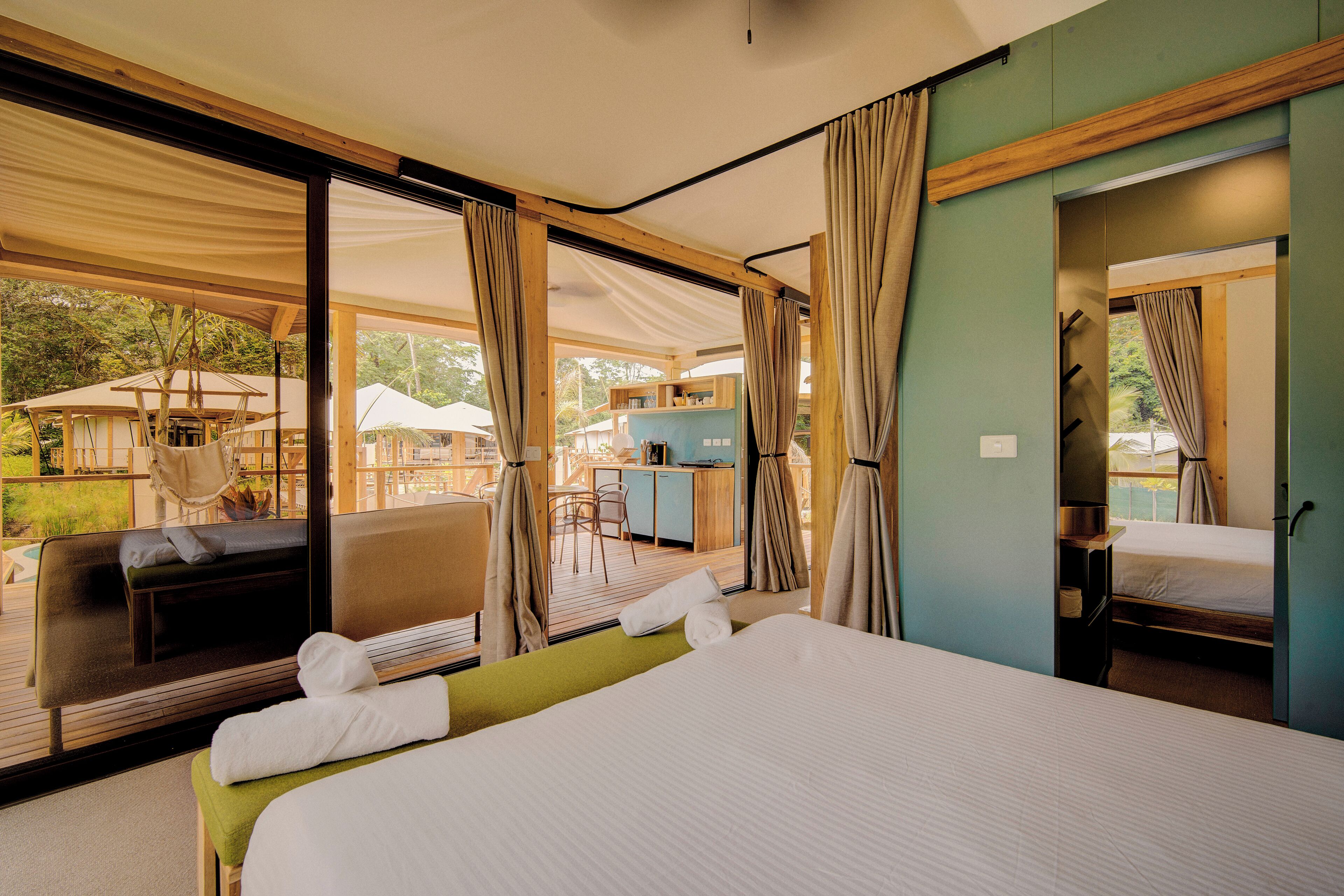 Een ruime kamer met een groot bed, een zithoek met een bank en stoelen, en uitzicht op een terras met parasols.