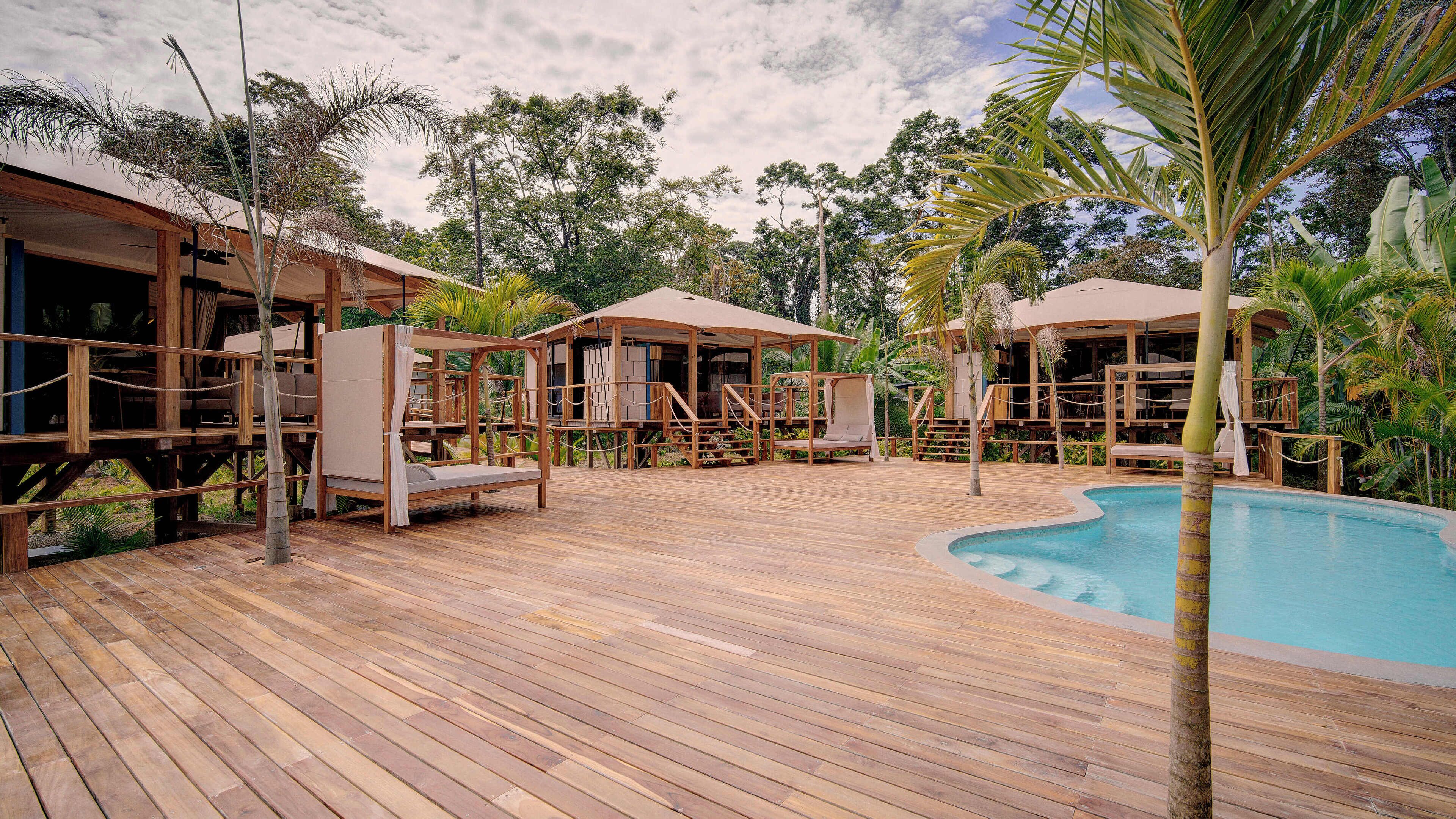 Um deck de madeira com piscina, cabanas de madeira e cadeiras de descanso.