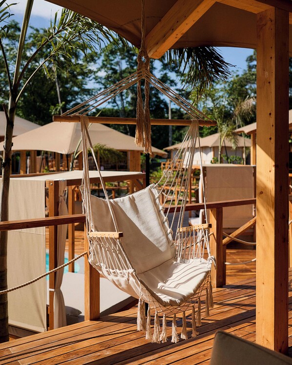 Una terraza de madera con una silla hamaca, mesas de madera y sombrillas.