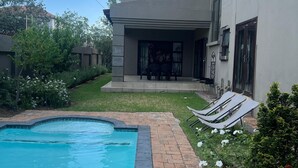 A modern house with a swimming pool, a patio with lounge chairs, and a well-maintained garden.