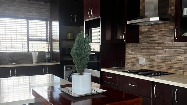 A modern kitchen with dark wood cabinets, a central island, and a backsplash with a stone pattern.