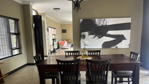 A dining area with a large rectangular table, six chairs, and a vase with a flower centerpiece.