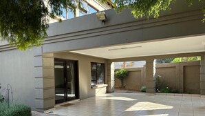 A covered outdoor area with a tiled floor, a sliding glass door, and a small garden with a tree and plants.
