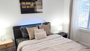 Ein Schlafzimmer mit Bett, Deckenventilator, Wandleuchte, Nachttisch, Fenster mit Vorhängen und einem Motivationsplakat.