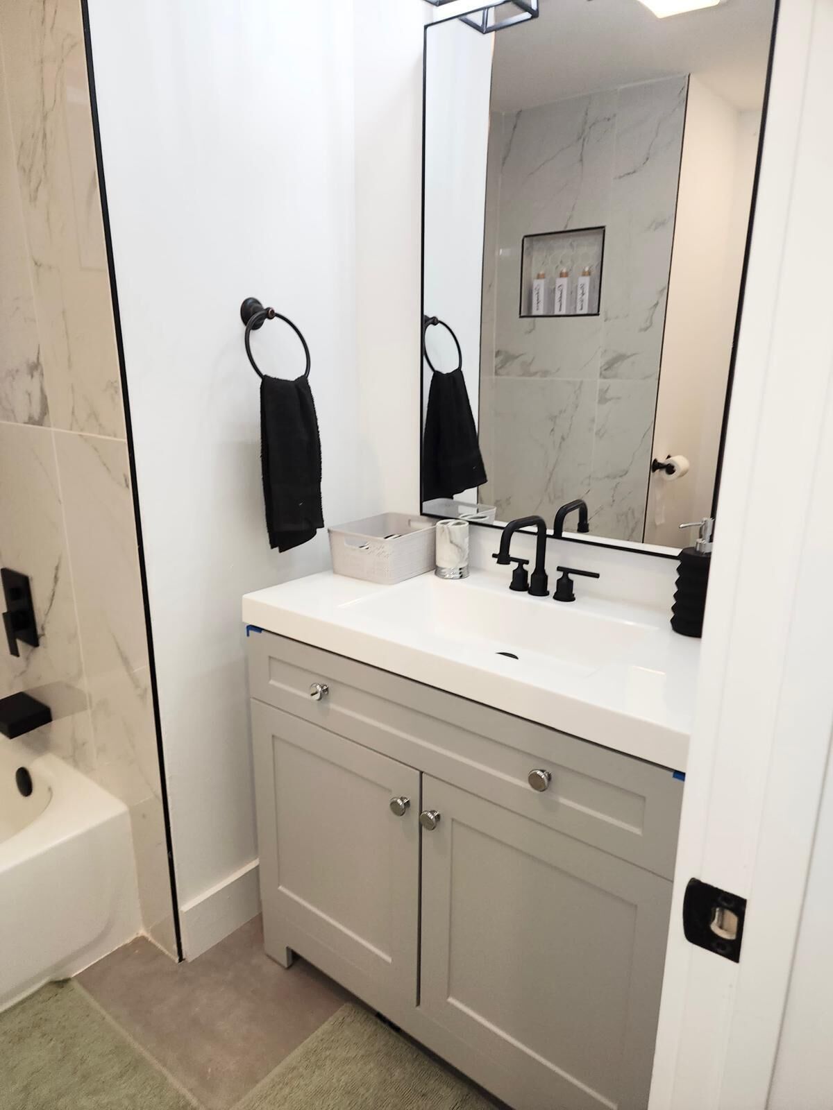Une salle de bain moderne avec un meuble-lavabo blanc, des porte-serviettes noirs, un grand miroir et des murs en marbre.
