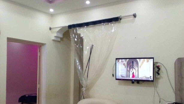 A living room with a beige armchair, a television mounted on the wall, and a patterned rug on the floor. - Dar Bilel a beautiful place  (Tozeur)