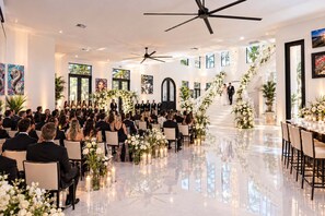 A formal event with guests seated facing a stage, a staircase with floral decorations, and a modern interior design.