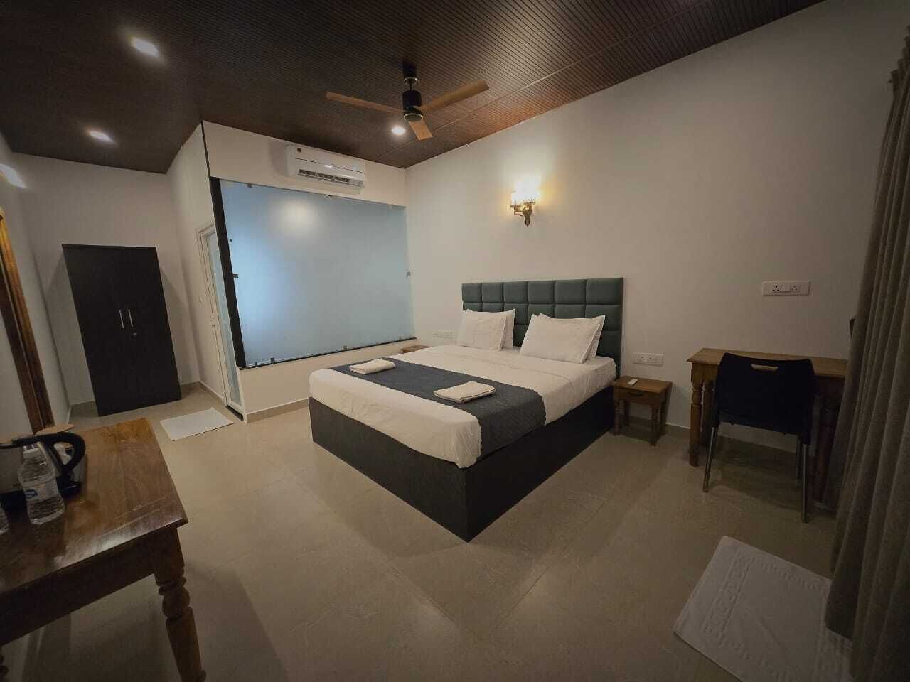 Una habitación de hotel con cama, escritorio, silla, armario y ventilador de techo.
