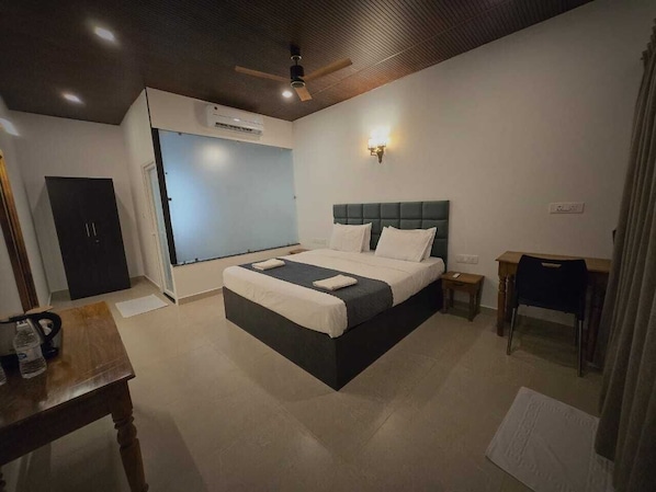 Una habitación de hotel con cama, escritorio, silla, armario y ventilador de techo.