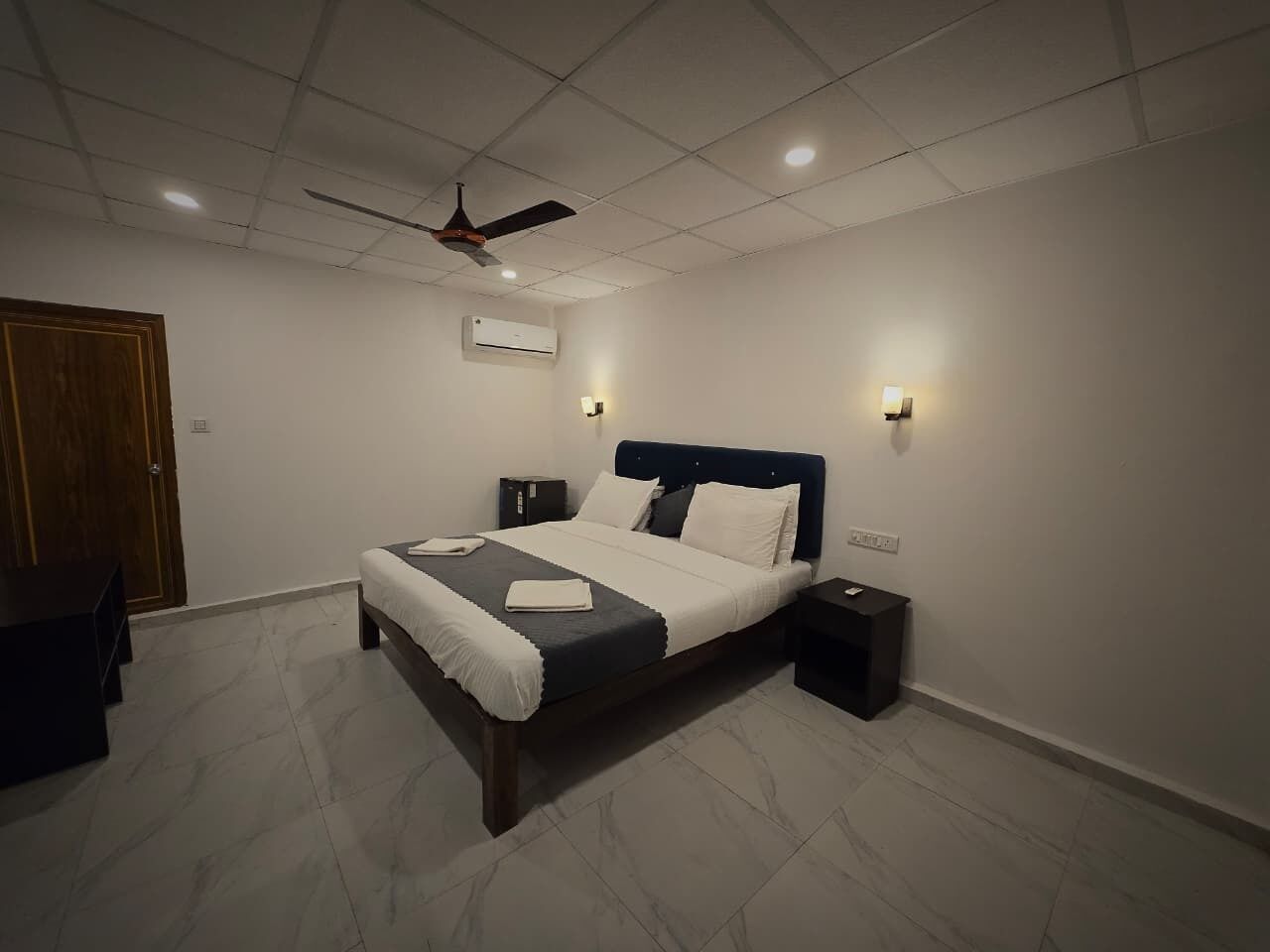 Un dormitorio con cama, mesitas de noche, ventilador de techo y aire acondicionado.